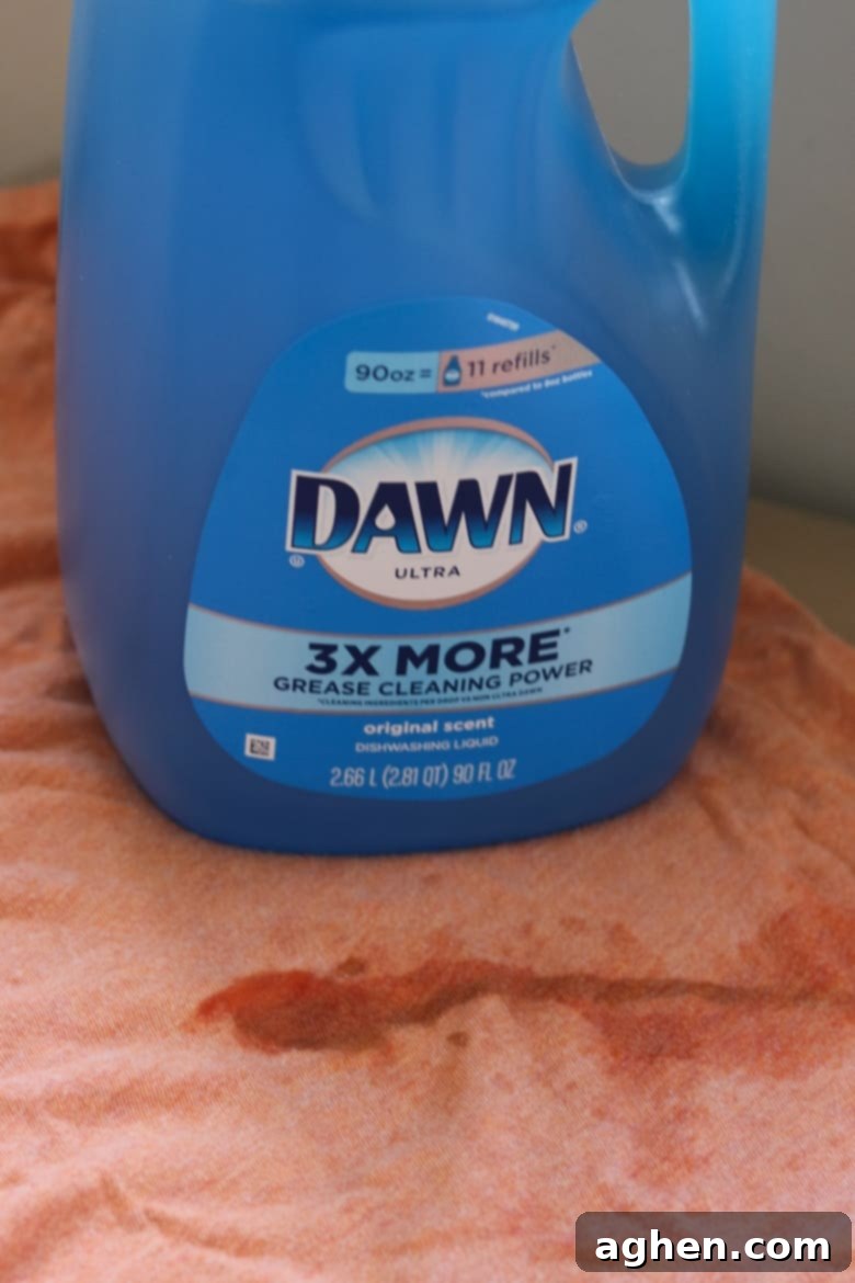 A bottle of blue Dawn dish soap placed on an orange shirt with a visible stain, illustrating its use as a laundry pre-treatment