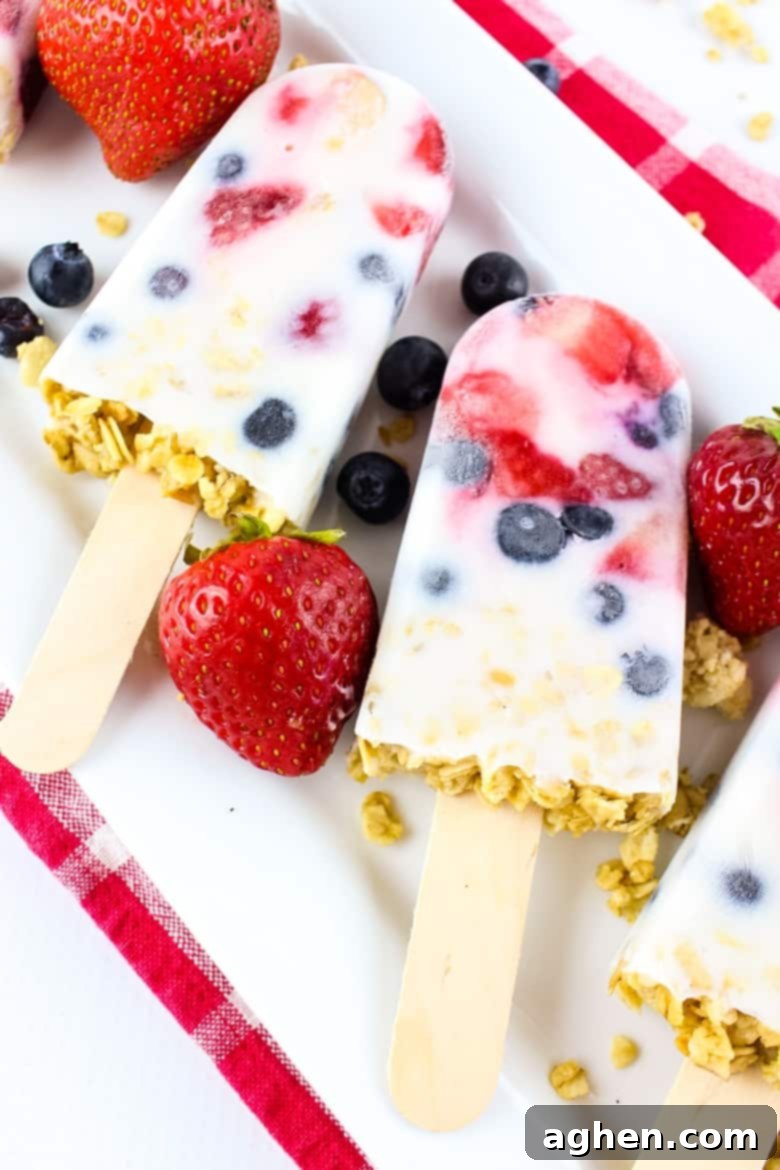 Yogurt, berry, and granola popsicles on a white platter, with fresh strawberries and blueberries
