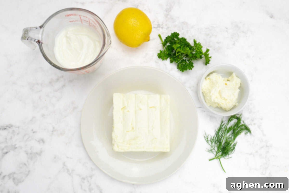 Party-Perfect Weight Watchers Whipped Feta Dip 3 The ingredients needed to make the dip are shown. A plate with a full bock of feta, a measuring cup with yogurt, a small bowl with cream cheese sit alongside herbs and a whole lemon.