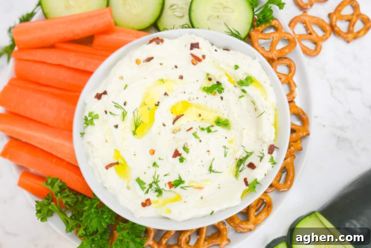 Party-Perfect Weight Watchers Whipped Feta Dip 6 An overhead view of the finished dip. On top of the dip are flakes of crushed red peppers, a light drizzle of oil and chopped herbs. The bowl sits on top of a plate filled with fresh cut veggies and pretzels.