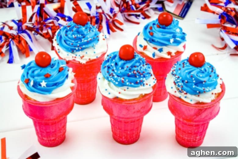 A close-up of festive 4th of July ice cream cone cupcakes, topped with swirls of white and blue icing and scattered patriotic sprinkles. These easy patriotic treats are great for kids and adults alike.