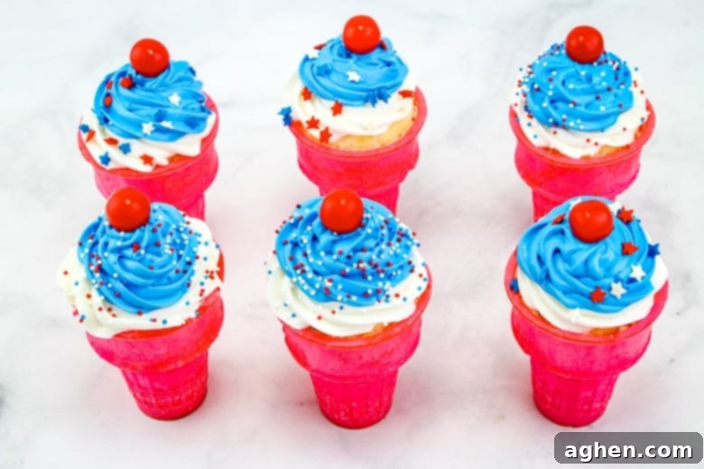 Finished red, white, and blue ice cream cone cupcakes, artfully decorated with patriotic sprinkles and a single red cherry candy on each, showcasing a perfect holiday dessert.