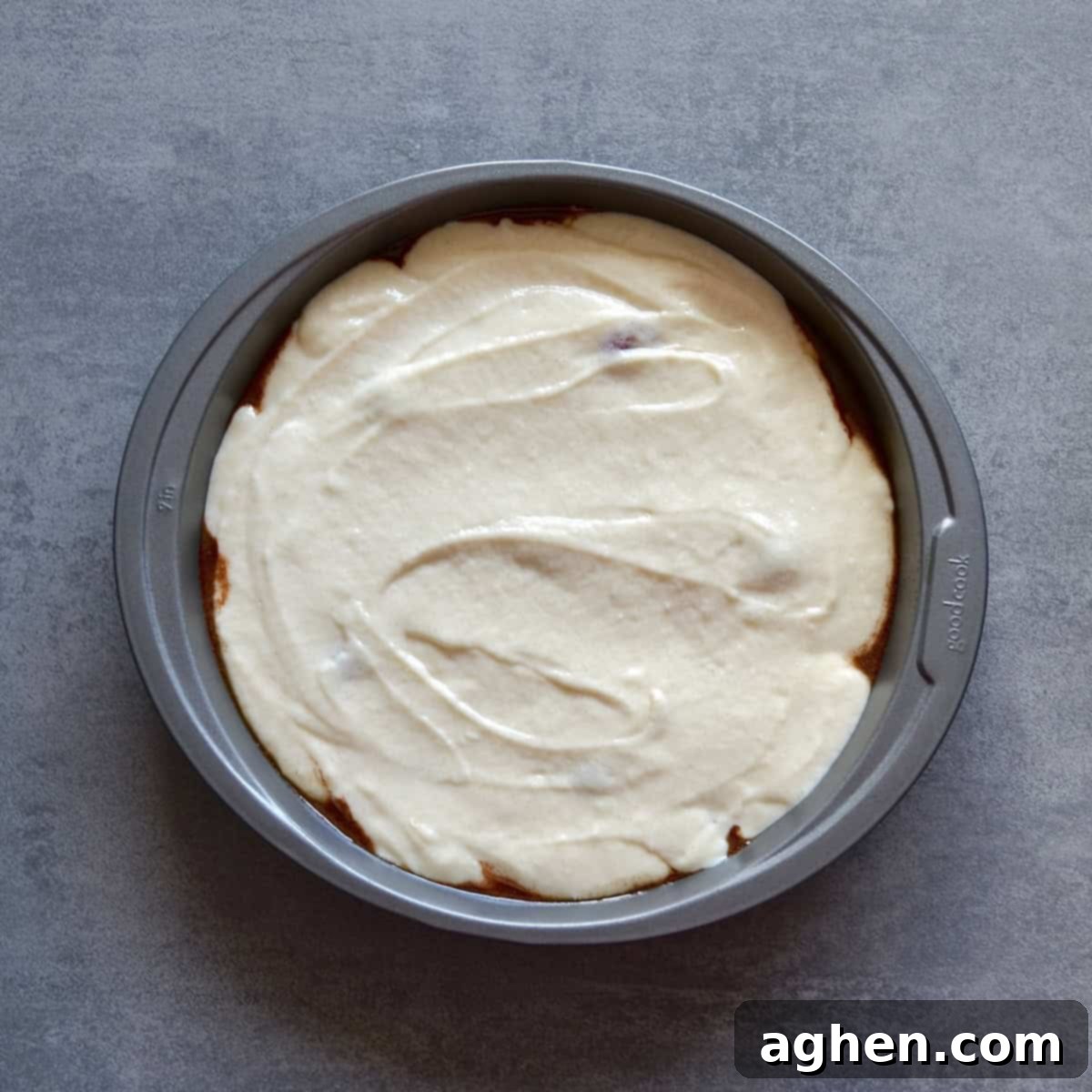 Cake batter spread evenly in a round cake pan over fruit