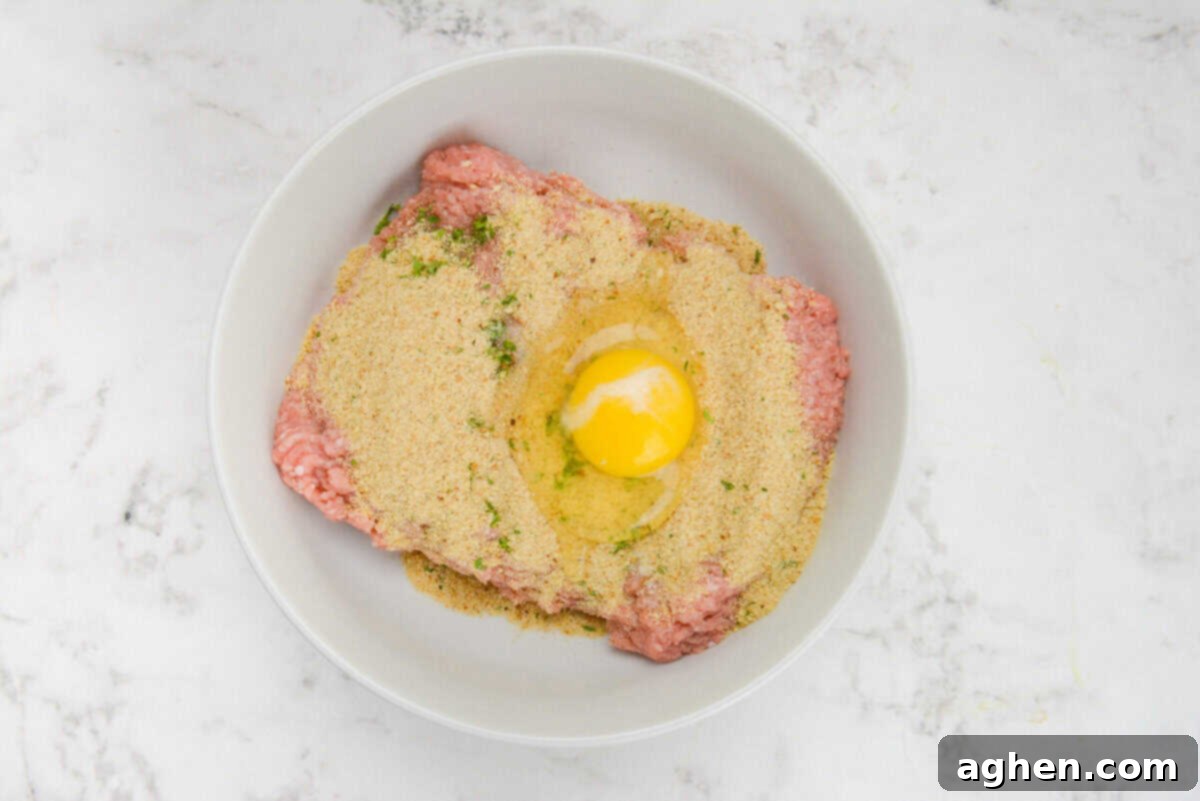 Zesty Greek Turkey Meatballs 5 A large white bowl filled with raw turkey. Breadcrumbs are sprinkled on top and an egg is cracked into the center but not yet mixed.