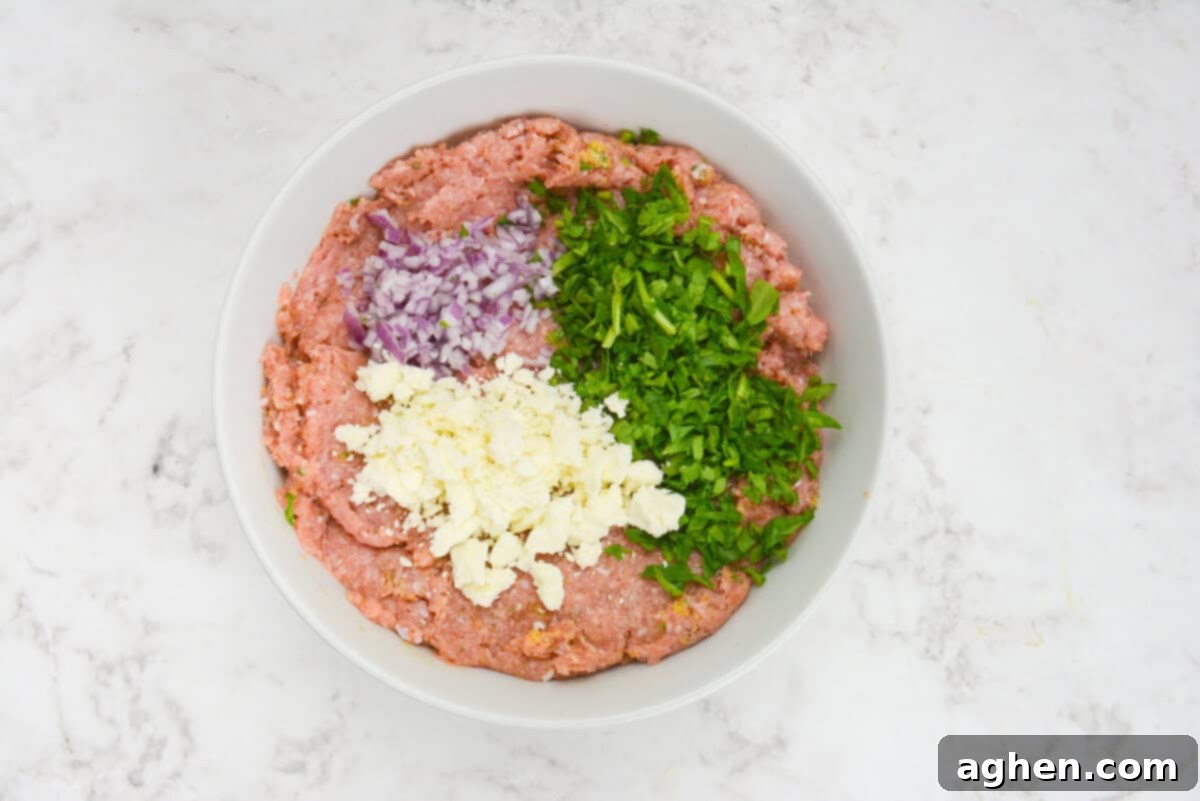 Zesty Greek Turkey Meatballs 6 A large white bowl with the mixed breadcrumbs and egg. On top is unmixed chopped spinach, feta and red onion.