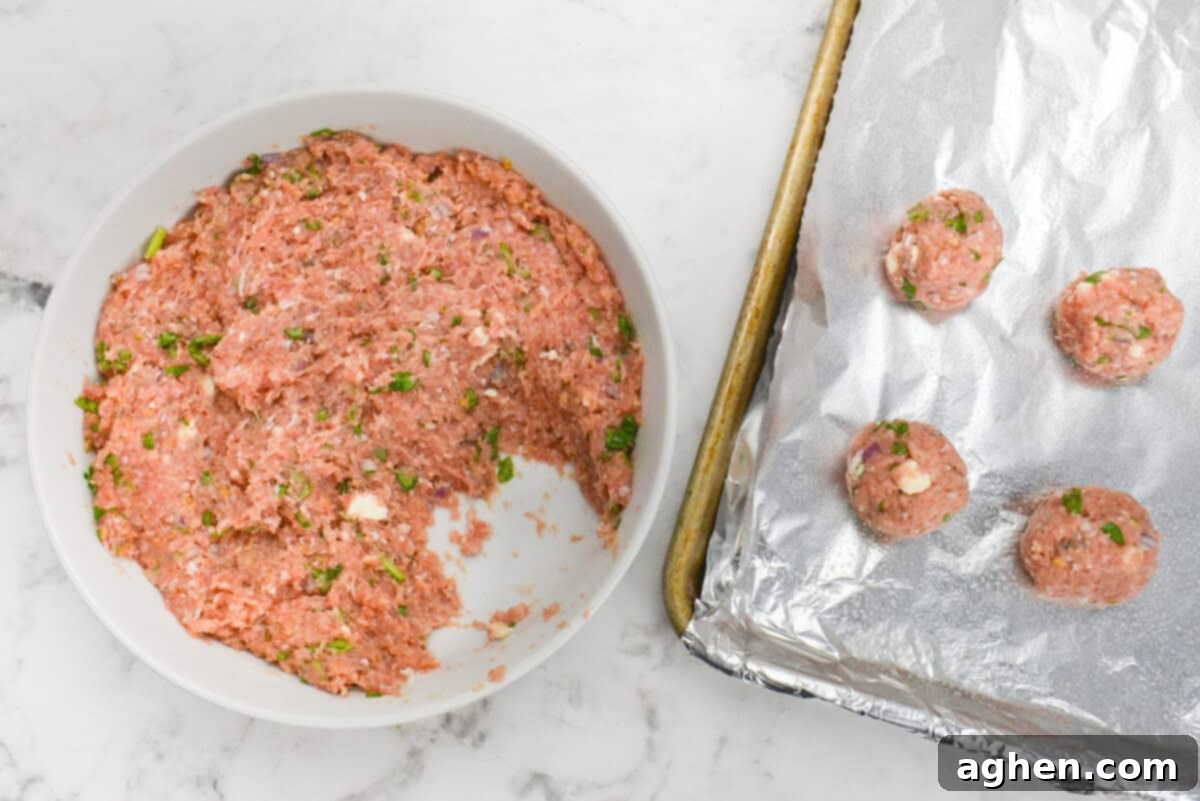 Zesty Greek Turkey Meatballs 7 A large white bowl is filled with the Greek turkey meatball mixture and scoops taken out. To the side is a foil lined baking sheet with four formed meatballs.