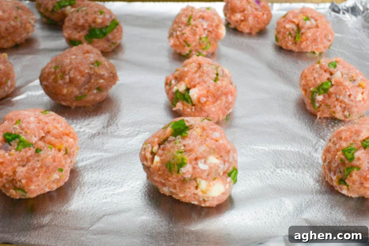 Zesty Greek Turkey Meatballs 8 A close up of the prepared meatballs on the baking sheet before going into the oven. The meatballs are speckled with spinach and chunks of feta.