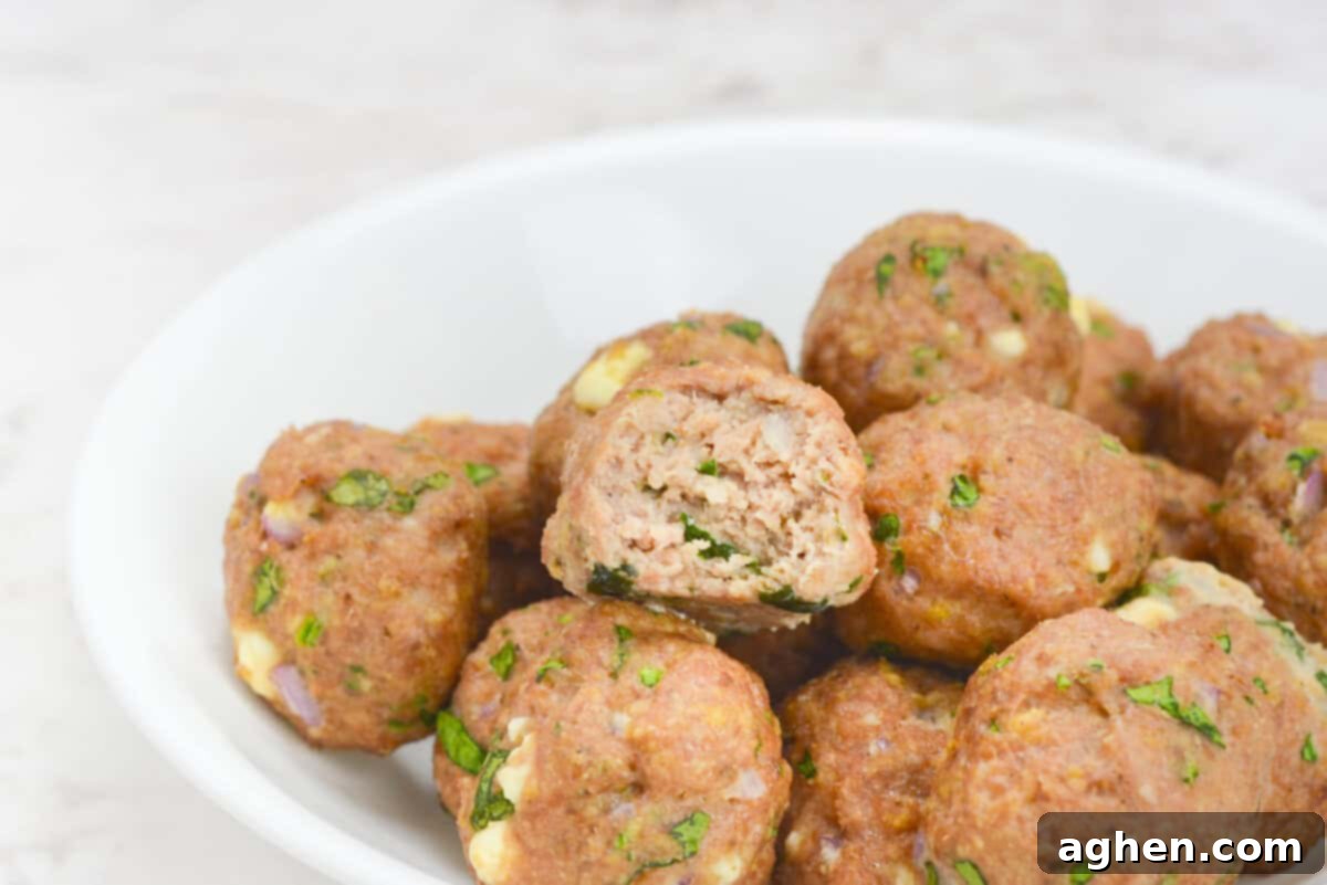 Zesty Greek Turkey Meatballs 9 A white bowl filled with baked meatballs in a small pile. One of the meatballs has a bite taken out.