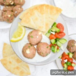 Zesty Greek Turkey Meatballs 10 An overhead view of a plate filled with baked meatballs sitting in a spoonful of tzatziki sauce. To the side is a lemon slice, pita, and a cucumber and tomato salad. In the background is an additional plate with the same ingredients, more pita and leftover meatballs.