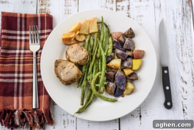 Pork loin medallions, fingerling potatoes, green beans, and apples on a white plate with plaid napkin and knife and fork.