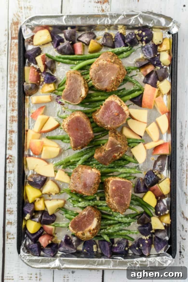 Uncooked pork tenderloin medallions with veggies on a sheet pan
