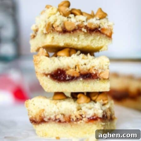 Nostalgic Peanut Butter & Jelly Squares 6 Close-up of a delicious Peanut Butter and Jelly Bar, revealing layers of a rich peanut butter cookie base, sweet fruit jam, and a crumble topping with melted peanut butter chips.