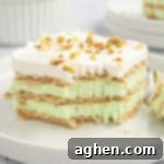 A slice of pistachio icebox cake with layers of graham crackers, green pistachio filling, and whipped topping, garnished with chopped pistachios.
