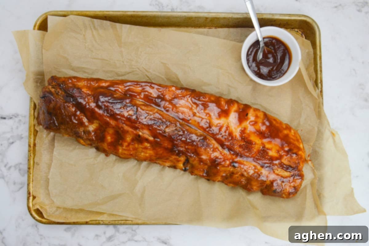 Achieving Perfect Ribs on Your Blackstone Griddle 13 An overhead of the finished rack of ribs on a brown parchment-lined baking sheet. A small bowl of sauce and a spoon sit to the side