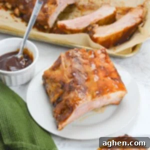 Achieving Perfect Ribs on Your Blackstone Griddle 14 A white plate with a portion of cooked ribs coated in barbecue sauce. To the side is a green textured napkin and a small bowl with sauce and a spoon. Above the plate sits a tray with sliced ribs.