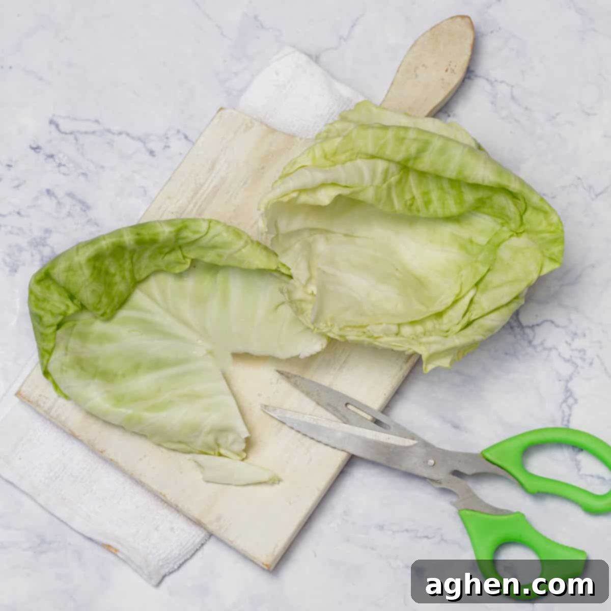 Individual cabbage leaves artfully arranged on a cutting board, with a pair of sharp kitchen scissors shown trimming the tough central stem and vein, preparing them for effortless rolling.