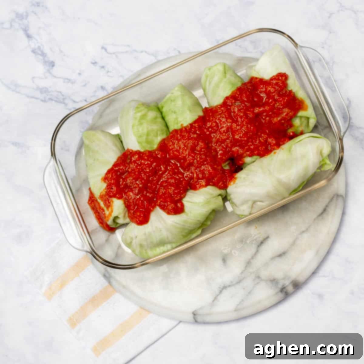 The assembled Pork Cabbage Rolls, neatly arranged and nestled in a ceramic baking dish, are generously covered with a vibrant marinara sauce, signaling their readiness for the oven.