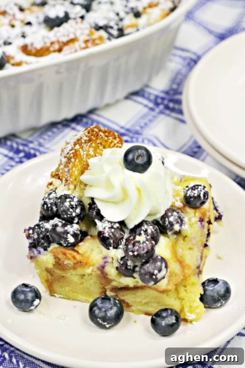 A generous slice of golden-brown Blueberry Croissant Breakfast Casserole, showcasing the fluffy, custard-soaked croissants and juicy blueberries, adorned with powdered sugar and ready to be served warm.