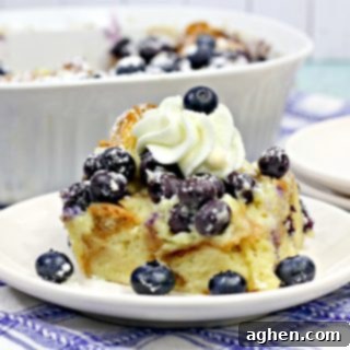 A beautifully plated slice of the Overnight Blueberry Croissant Breakfast Bake, adorned with fresh blueberries and a generous dollop of whipped cream, inviting a bite.