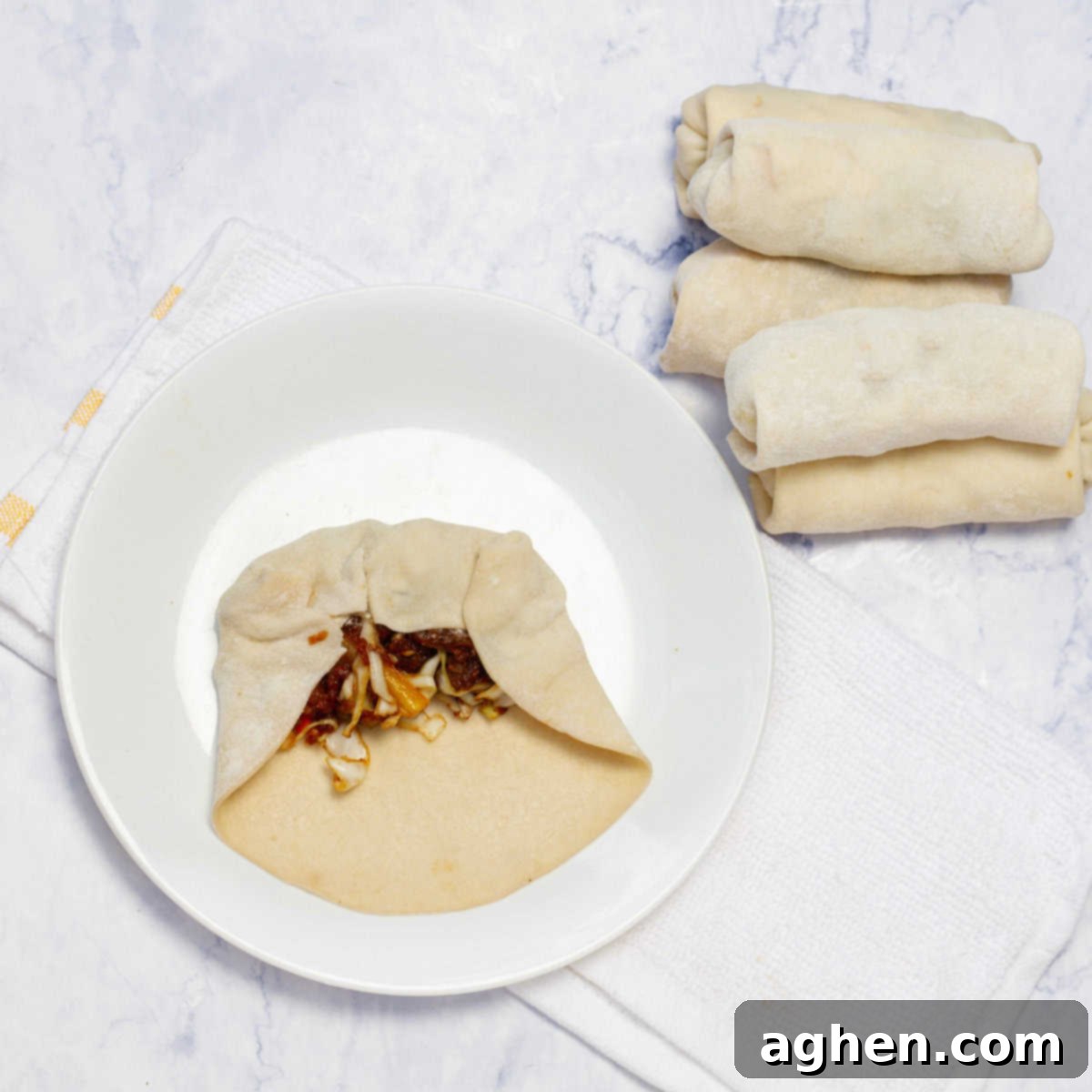 Ditch Takeout for These Weight Watchers Pork Egg Rolls 6 The initial fold of an egg roll wrapper over the filling, demonstrating how the bottom corner is tucked in tightly to begin the rolling process.