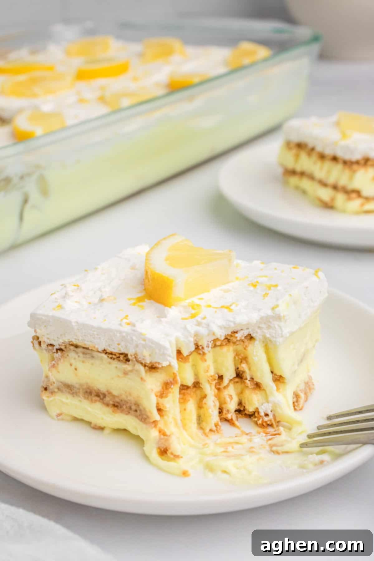 Slice of lemon Icebox cake with bite taken out of it, showing layers of creamy lemon pudding and soft graham crackers.