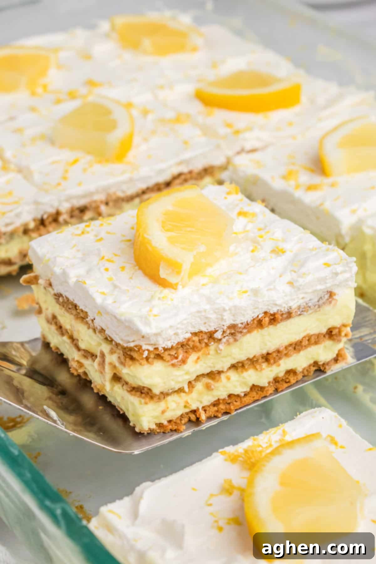 Square slice of the layered lemon pudding dessert being lifted from the baking dish with metal spatula.