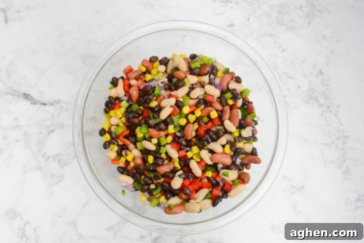 A large clear mixing bowl filled with all of the vegetables and beans