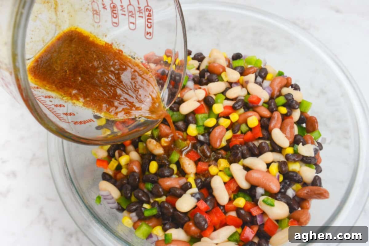 A 45 degree angle close up of the dressing being poured over the Mexican three bean salad 