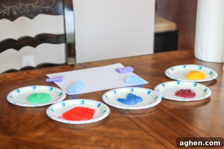 A creative setup for toddler art: homemade taste-safe paints on paper plates, blank paper, and an assortment of cut kitchen sponges, ready for painting.