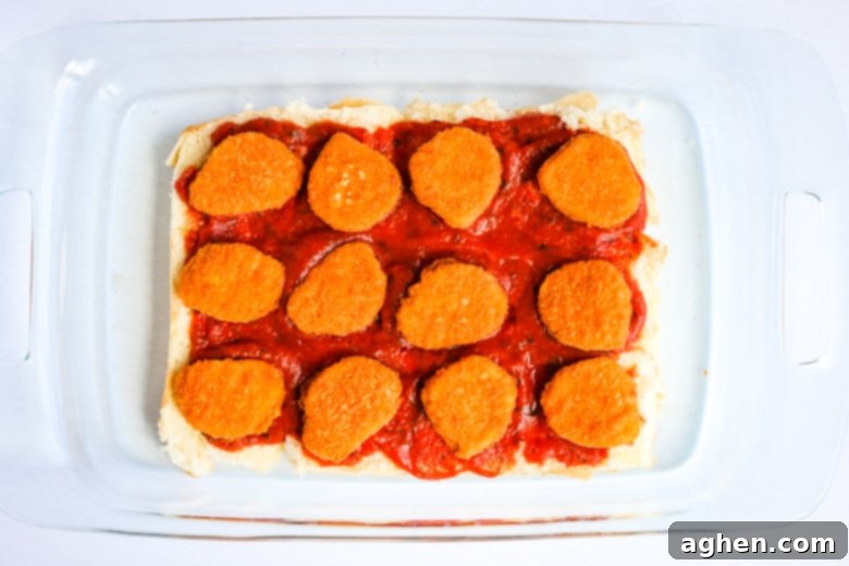 12 Hawaiian rolls in a casserole dish topped with marinara sauce and chicken nuggets.