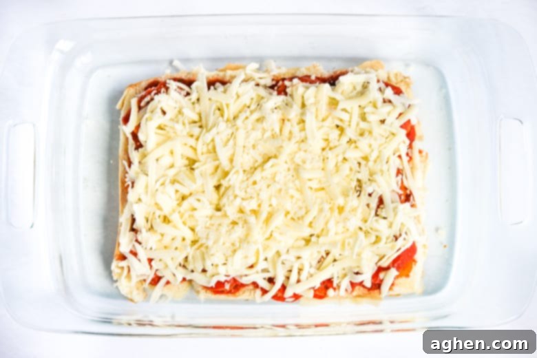 Sliders buns topped with tomato sauce, nuggets, and shredded cheese.