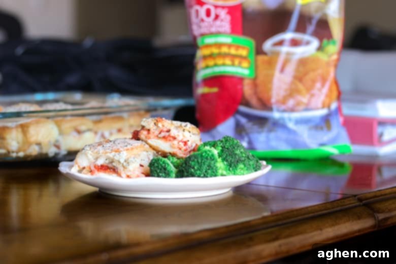 Chicken Parm Sliders served with broccoli on a white plate. Bag of frozen chicken nuggets and glass baking dish with remaining sliders are in the background.