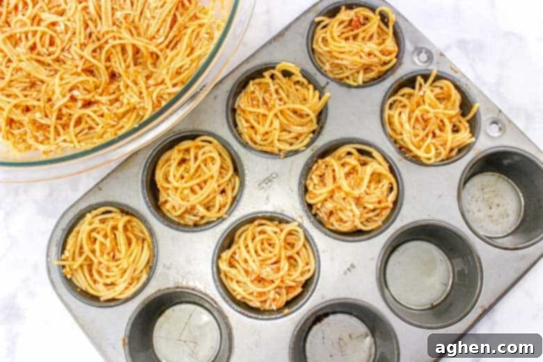 muffin tin filled with spaghetti, forming nests for spaghetti and meatball cups