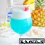 Frozen blue cocktail garnished with fresh pineapple and maraschino cherry