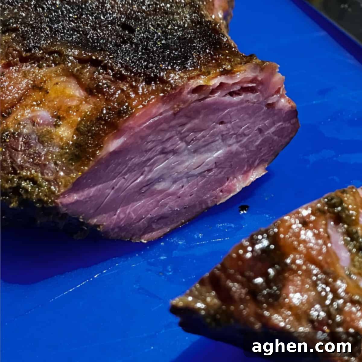 Smoked tri-tip being thinly sliced against the grain on a blue cutting board, revealing its tender, juicy interior after resting for 30 minutes.
