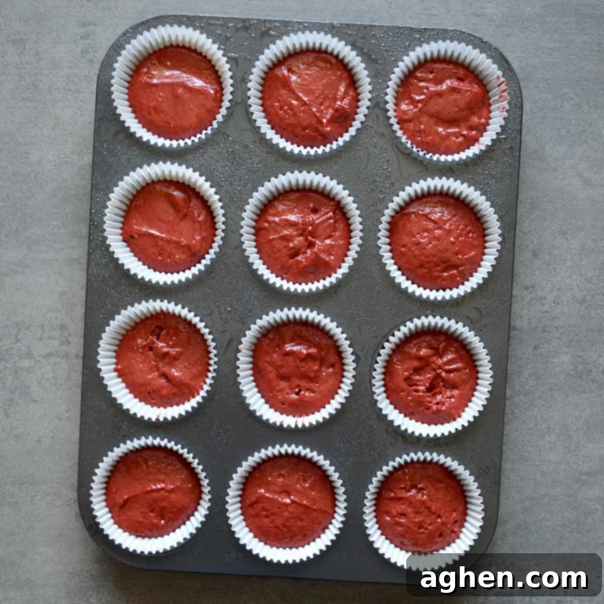 Red velvet cupcake batter scooped into a muffin pan.