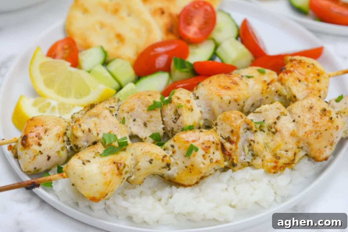 A close-up shot of perfectly cooked chicken souvlaki skewers resting on a bed of seasoned rice. In the softly blurred background, vibrant lemon wedges, a refreshing cucumber and tomato salad, and warm flatbread complete the Mediterranean feast, ready to be enjoyed.