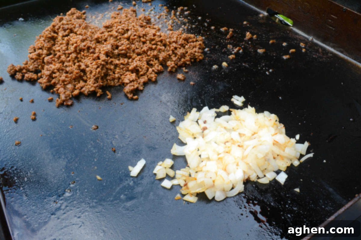The Ultimate Blackstone Nacho Recipe 7 A close-up view of ground beef perfectly mixed with taco seasoning, alongside translucent, cooked white onions on the griddle.