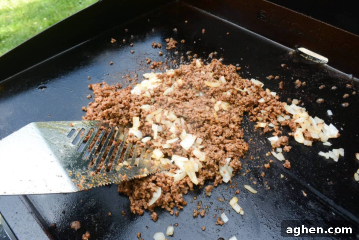 The Ultimate Blackstone Nacho Recipe 8 The seasoned ground beef and softened onions are mixed together expertly with a silver grill spatula on the Blackstone griddle.