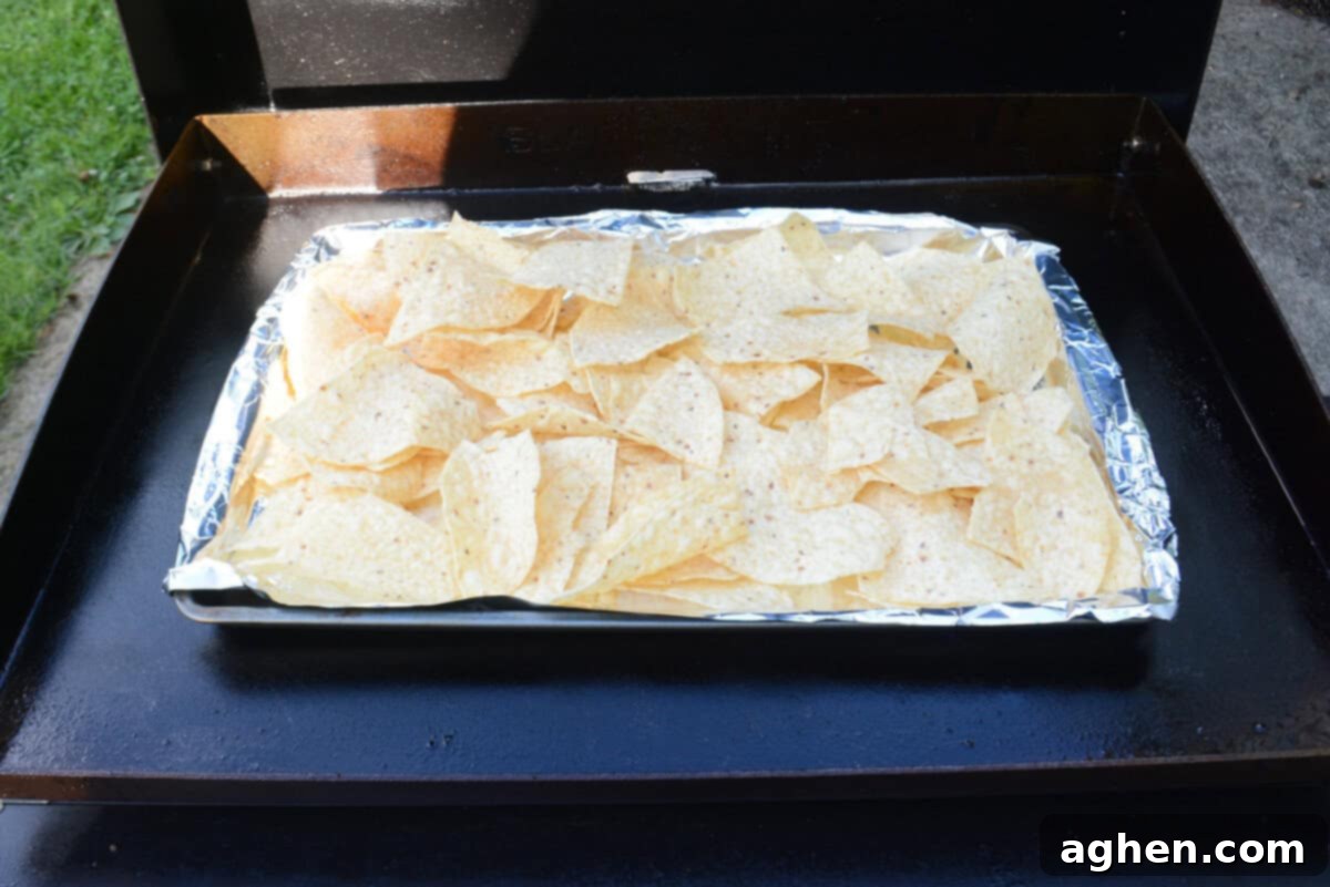 The Ultimate Blackstone Nacho Recipe 9 A sheet pan, covered in aluminum foil and piled high with tortilla chips, is carefully placed directly onto the Blackstone griddle.