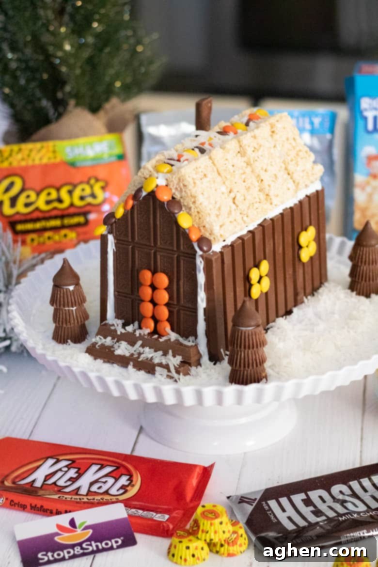 A beautifully decorated Christmas candy house constructed from KitKat Bars, Hershey's Bars, Reese's Pieces, Reese's Peanut Butter Cups, and Rice Krispies Treats, set against a festive background.