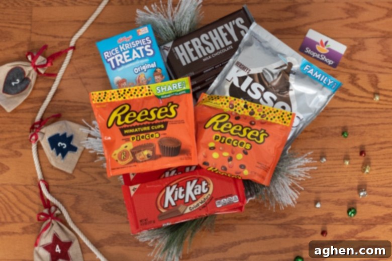An array of candy cabin supplies including Rice Krispie Treats, Reese's Pieces, Reese's Peanut Butter Cups, Kit Kat Bars, Hershey bars, and Hershey Kisses, ready for construction.