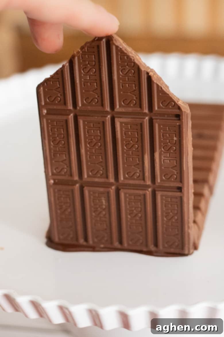 A chocolate Hershey bar wall being carefully attached to the Kit Kat bar base, illustrating the initial construction phase of the candy cabin.