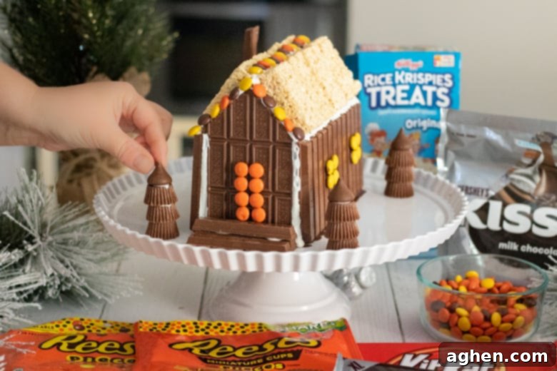 A close-up of adding Hershey's Kisses as the final touch to Reese's Peanut Butter Cup trees, enhancing the festive candy cabin scene.