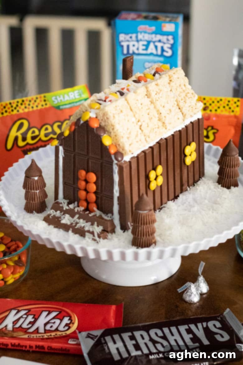 An elaborate Christmas candy house, expertly constructed with chocolate bars, Kit Kats, Reese's Peanut Butter Cups, Hershey's Kisses, and Rice Krispie Treats, making a grand festive statement.
