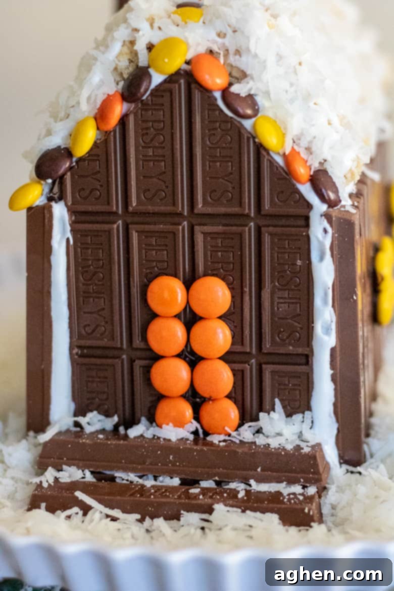 The charming front facade of the Candy Cabin, featuring an inviting orange Reese's Pieces front door and meticulously arranged Kit Kat steps, surrounded by festive candy decorations.