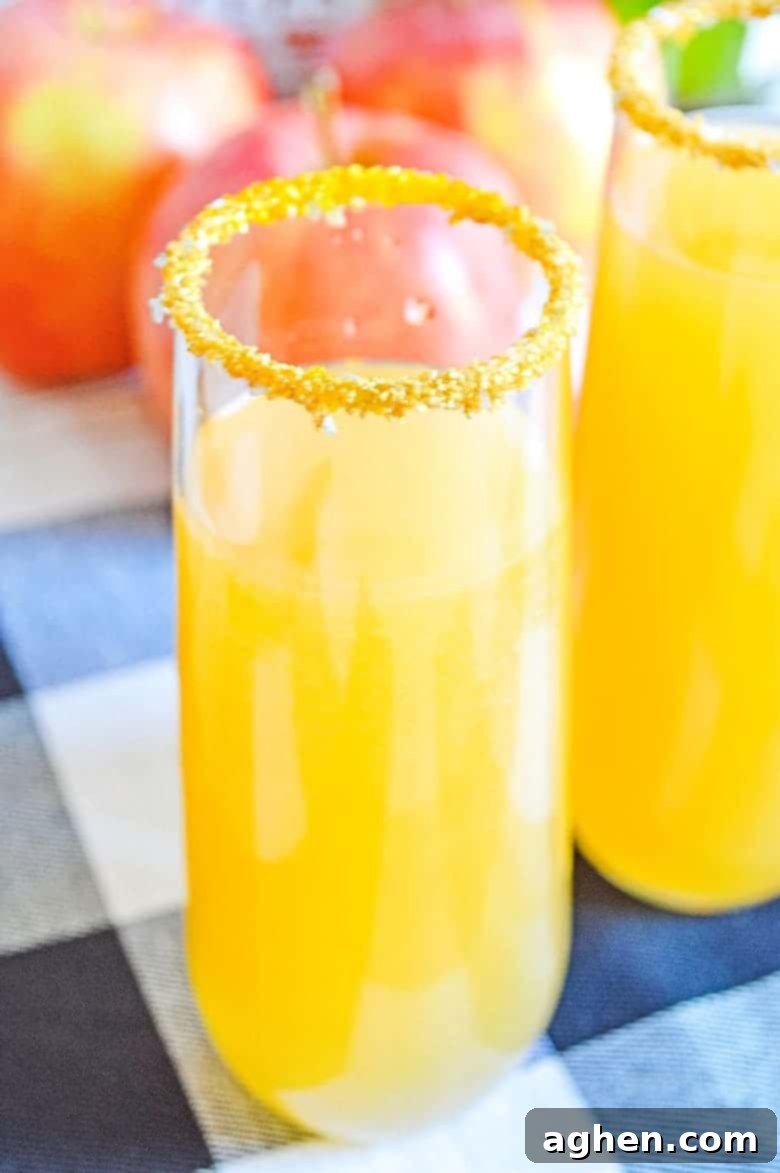 Two sparkling apple cider mimosas garnished with apple slices on a rustic wooden table, ready for a fall celebration.