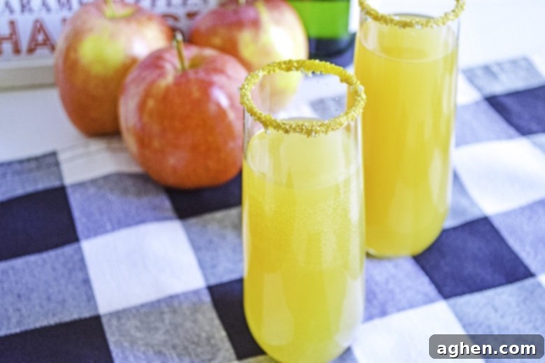 A pair of beautifully garnished apple cider mimosas on a table, with autumn decor in the background, exuding a festive atmosphere.