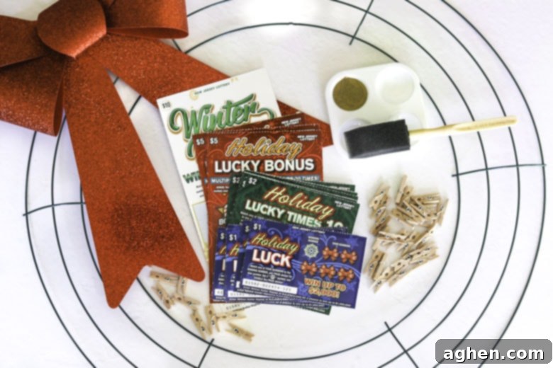 Supplies laid out for making a lottery ticket wreath: metal wreath form, instant lottery tickets, red bow, miniature clothespins, gold paint, and a foam brush.
