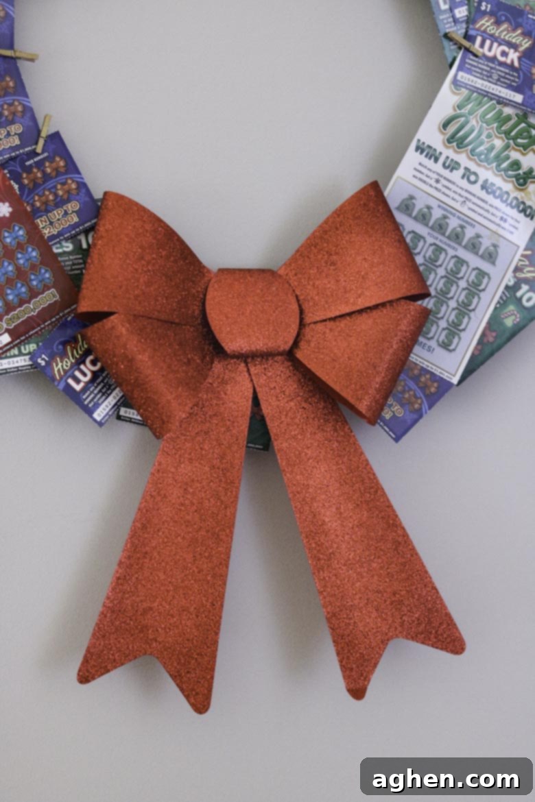 A vibrant Christmas lottery ticket wreath featuring a large red bow attached to the bottom, adding a festive touch to the unique gift.
